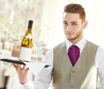 male waiter holding a tray with bottle of wine and glasses